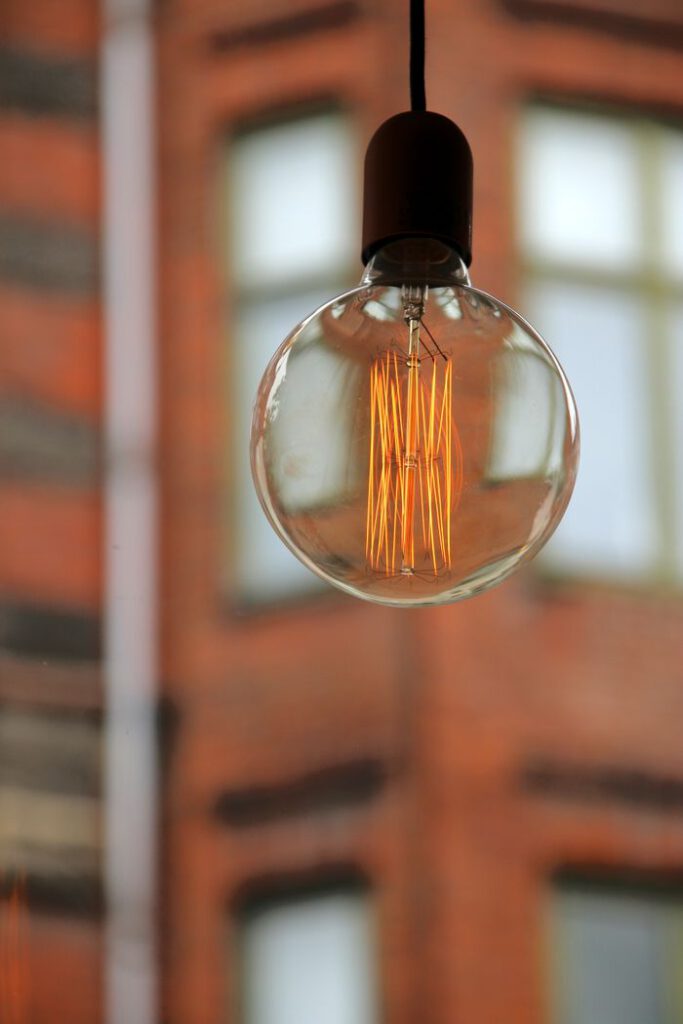 A round light bulb brightly illuminated, hanging indoors with a blurred brick background.
